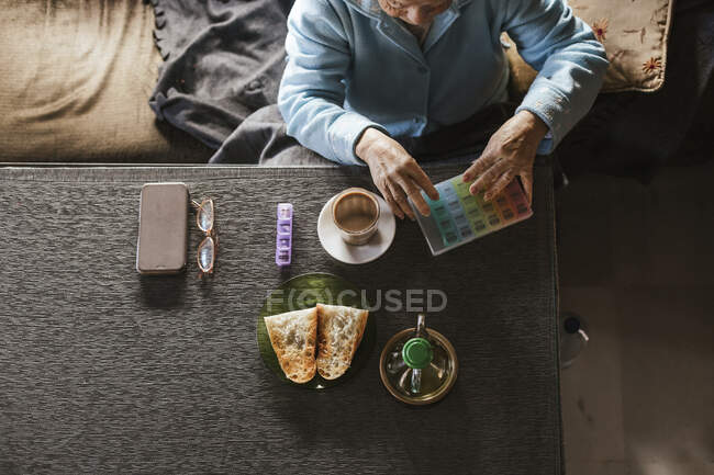 Donna anziana con contenitore di medicinali sul tavolo a casa — Foto stock