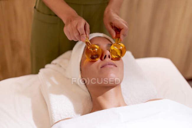 Masajista sosteniendo globos de vidrio en la cara del cliente femenino en el spa de salud - foto de stock