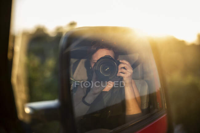 Spiegelbild einer Frau, die die untergehende Sonne fotografiert — Stockfoto