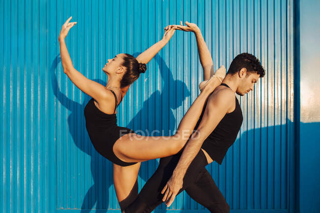 Gymnaste professionnel couple faisant attitude équilibre pose par mur bleu — Photo de stock