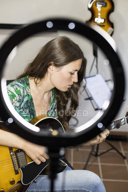 Молодая женщина с веб-камеры свет играет на гитаре, сидя дома — стоковое фото