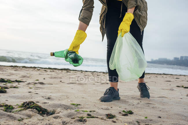 Ambientalista con la playa de limpieza de bolsas de basura mientras está de pie contra el cielo despejado - foto de stock