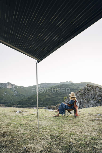 Donna che indossa il cappello seduta sulla sedia mentre guarda lontano durante le vacanze — Foto stock