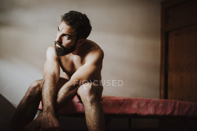 Pensativo hombre desnudo mirando hacia otro lado mientras está sentado en la cama - foto de stock