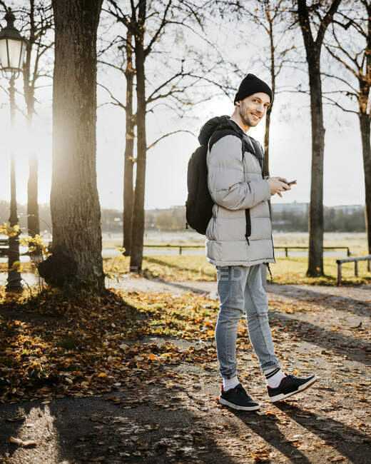 Uomo che tiene lo smart phone mentre cammina nel parco durante l'autunno — Foto stock