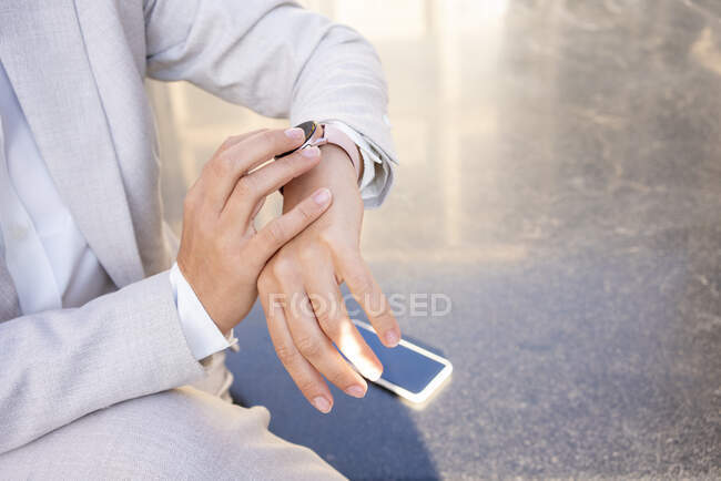 Mujer comprobando el tiempo en reloj de pulsera mientras está sentado en el banco de la ciudad - foto de stock