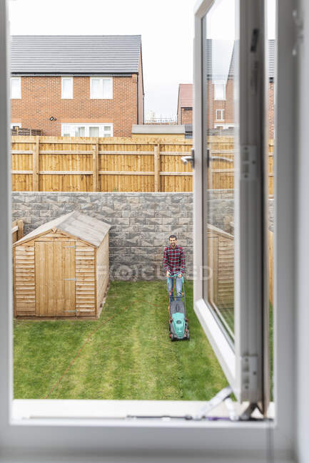 Ventana abierta con el hombre segando patio trasero en el fondo - foto de stock