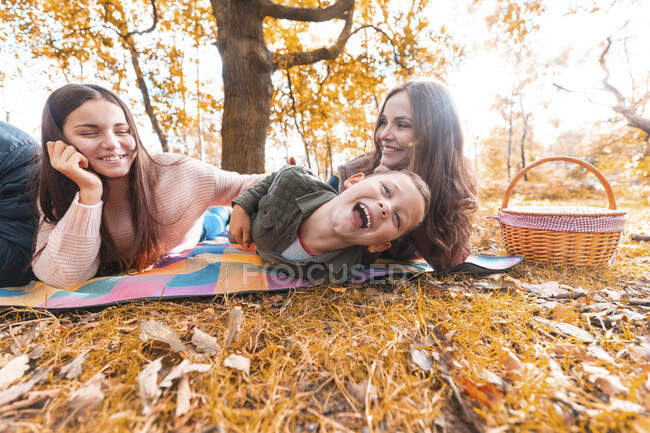 Familia sonriente disfrutando tumbada en el parque durante el otoño - foto de stock