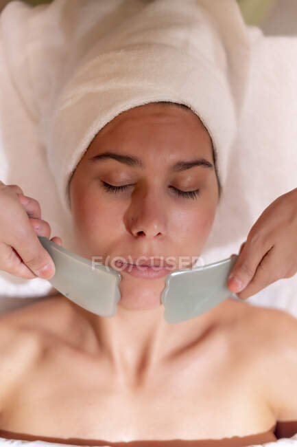 Esteticista sosteniendo gua sha en la barbilla del cliente femenino en el spa de salud - foto de stock