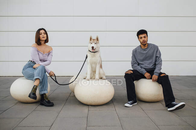 Хлопець і дівчина сидять на собаці з соціальною відстанню на білому бетонному м'ячі до стіни. — стокове фото