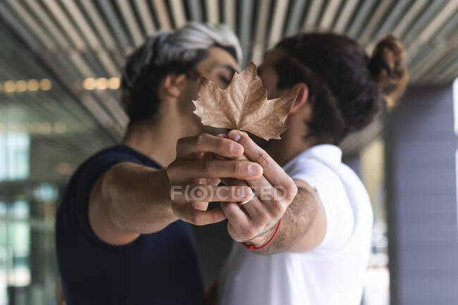 Homosexual pareja mostrando arce hoja mientras besos en ciudad - foto de stock