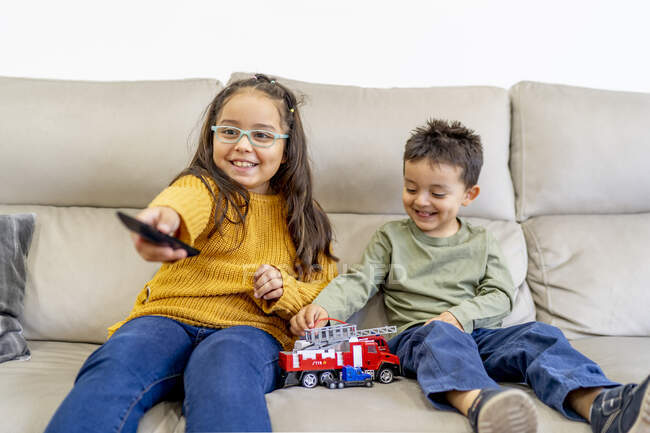 Schwester schaut fern, während Bruder zu Hause auf Sofa mit Feuerwehrspielzeug spielt — Stockfoto