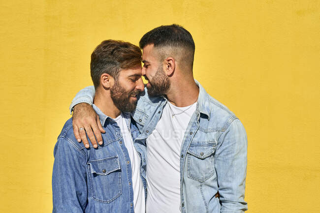 Sorrindo gay casal de pé com braço em torno de pé contra amarelo parede — Fotografia de Stock