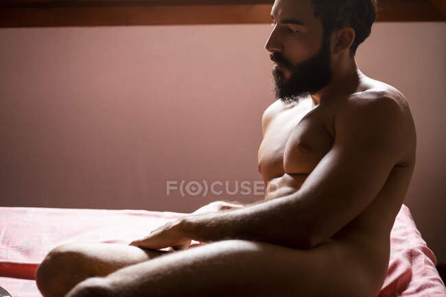 Joven hombre desnudo sentado en la cama en casa - foto de stock