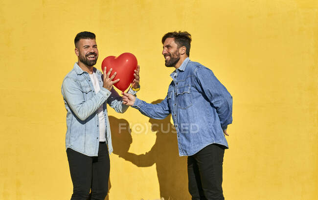 Человек, дающий сердечный шар геям, стоя напротив желтой стены — стоковое фото