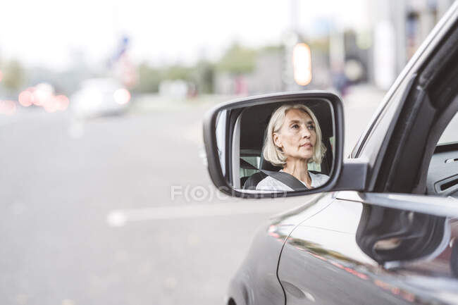 Spiegelbild einer Geschäftsfrau im Seitenspiegel am Steuer eines Autos in der Stadt — Stockfoto
