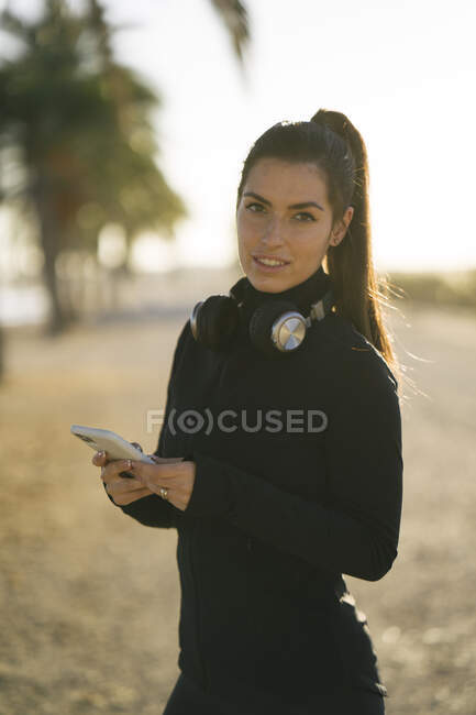 Mujer joven usando el teléfono inteligente mientras está de pie contra el cielo despejado al atardecer - foto de stock