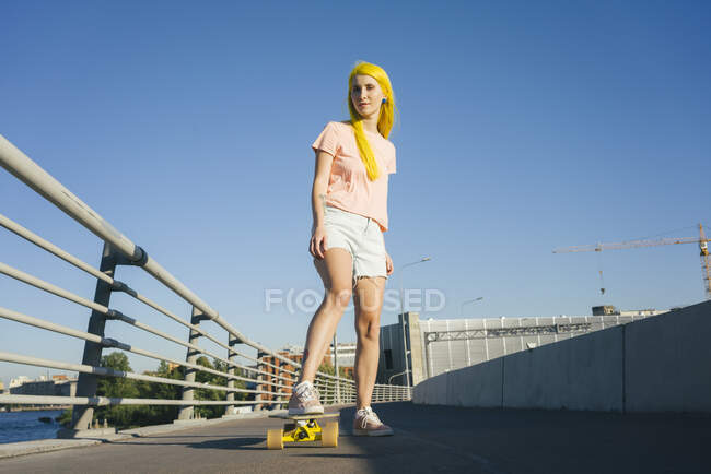 Frau steht bei sonnigem Wetter auf Skateboard gegen Kahlschlag — Stockfoto