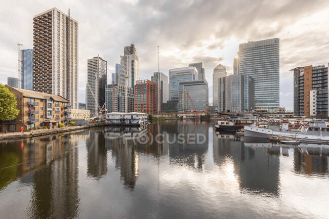 Bateaux amarrés au port près des gratte-ciel modernes en ville contre un ciel nuageux au coucher du soleil, Londres, Royaume-Uni — Photo de stock