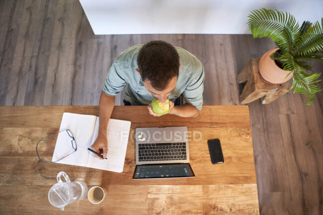 Мужчина-фрилансер ест свежее яблоко, работая дома — стоковое фото