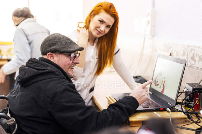 Lächelnder Mann mit Laptop von Pflegerin in Behindertenzentrum — Stockfoto