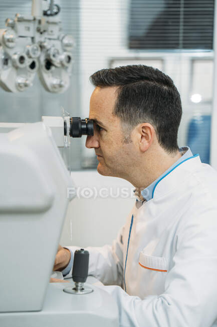 Чоловік - оптик виглядає у клініці фороптером. — стокове фото