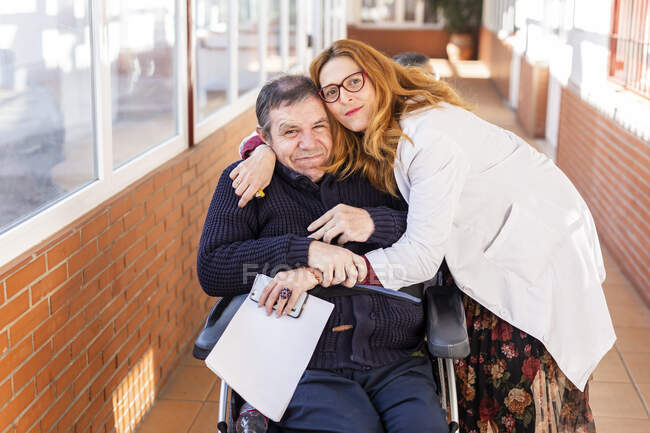 Femme soignante embrassant un homme handicapé assis en fauteuil roulant dans une maison de soins infirmiers — Photo de stock