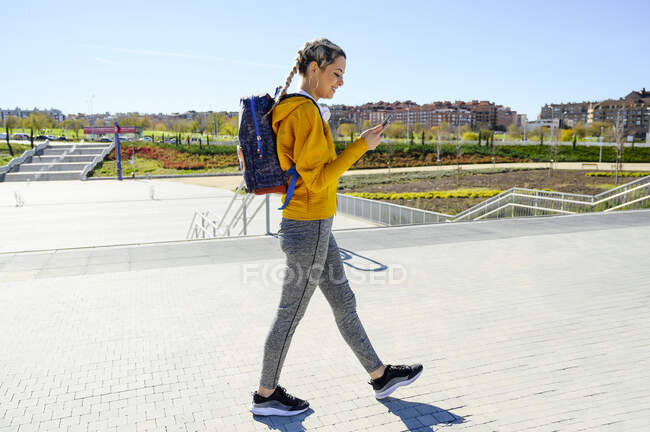Athlète féminine avec sac à dos utilisant un téléphone portable tout en marchant sur le sentier — Photo de stock
