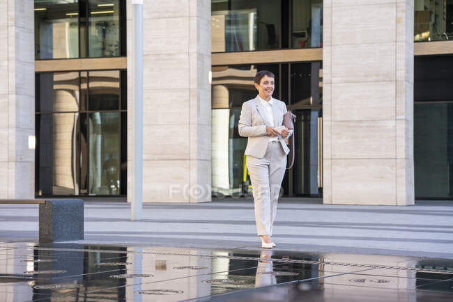 Businesswoman holding purse while standing by fountain in city — Stock Photo