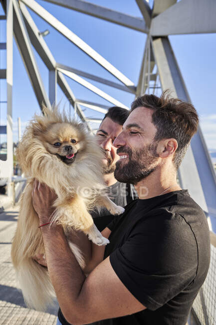 Homosexual couple with dog on footbridge during sunny day — Stock Photo