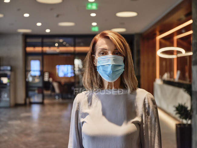 Старшая женщина в защитной маске стоит в вестибюле отеля — стоковое фото