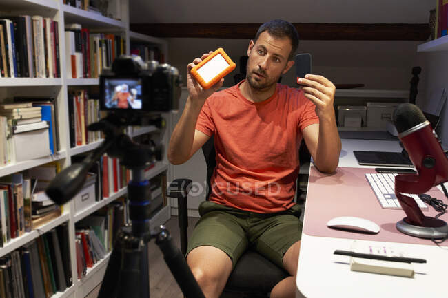 Metà uomo adulto che mostra disco rigido esterno mentre la registrazione video sulla fotocamera a casa — Foto stock