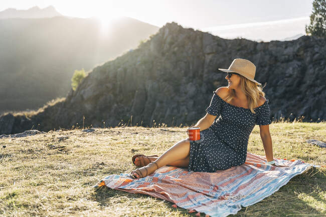 Lächelnde Frau mit Kaffeetasse träumt am sonnigen Tag auf Picknickdecke — Stockfoto