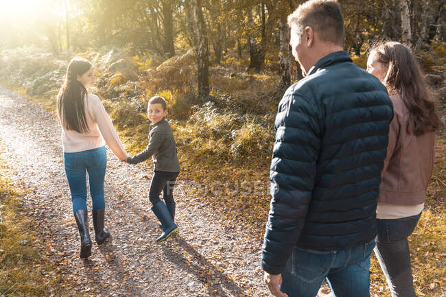 Siblings looking over shoulder at parents walking behind in park during autumn — Stock Photo