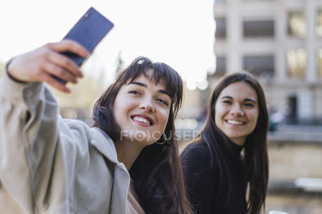 Jovem feliz tomando selfie amigo feminino enquanto passeia — Fotografia de Stock
