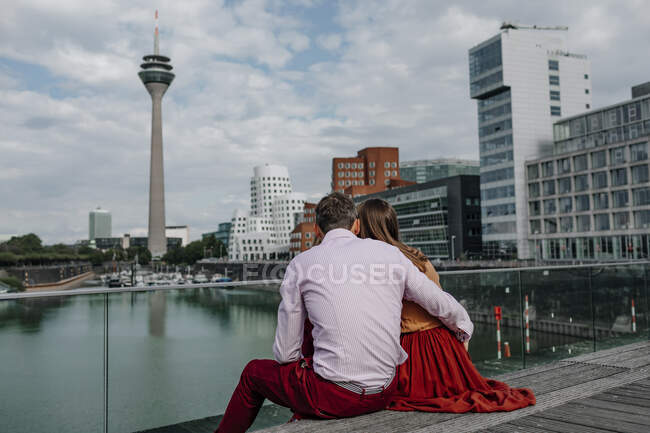 Casal heterossexual abraçando enquanto sentado na ponte na cidade — Fotografia de Stock