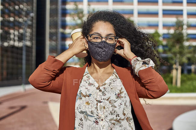 Giovane donna con maschera protettiva in piedi in città nella giornata di sole — Foto stock