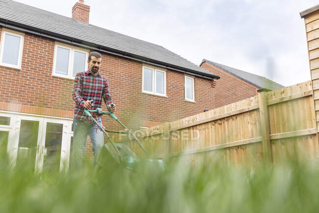 Человек стрижет газон газонокосилкой на заднем дворе — стоковое фото