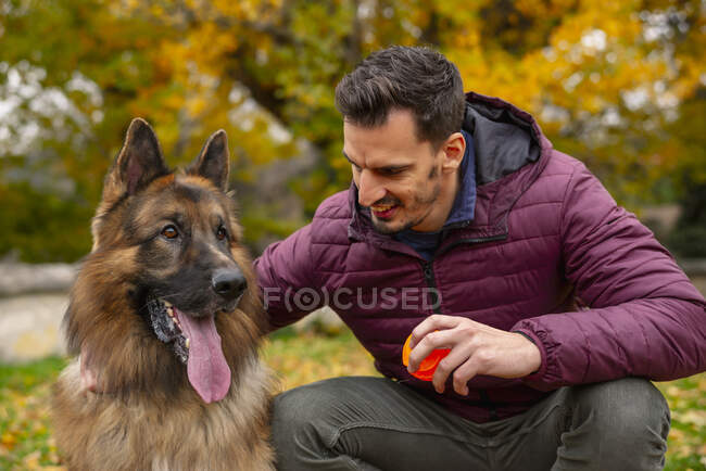 Uomo sorridente con giocattolo guardando il cane mentre accovacciato al parco — Foto stock