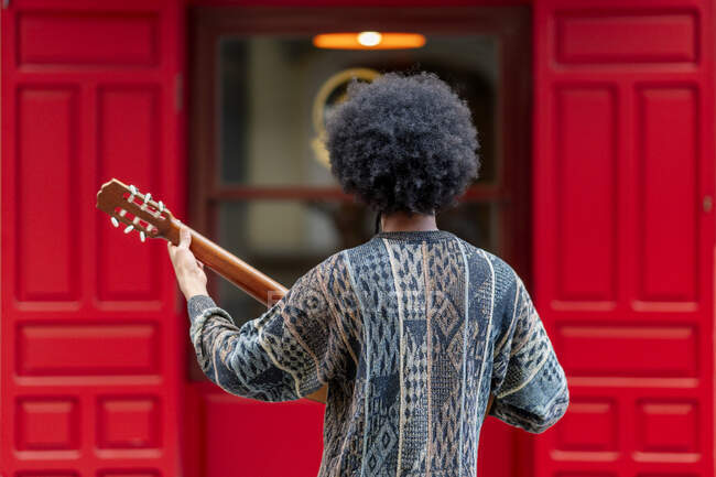 Молодий чоловік грає на гітарі, стоячи перед будівлею — стокове фото