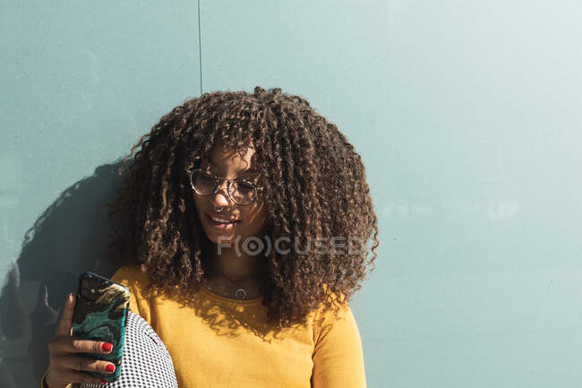 Sorridente giovane donna utilizzando smartphone contro vetro nella giornata di sole — Foto stock