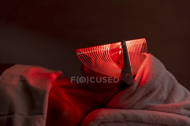 Young woman wearing red mask during rejuvenating treatment in dark at beauty spa — Stock Photo