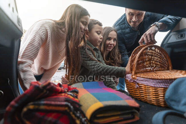 Lächelnde Familie holt Picknicksachen aus dem Kofferraum — Stockfoto