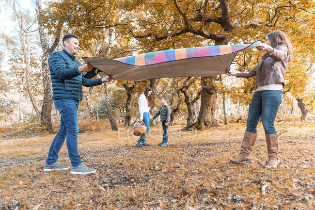 Genitori sdraiati coperta picnic mentre i bambini in piedi dietro nel parco durante l'autunno — Foto stock