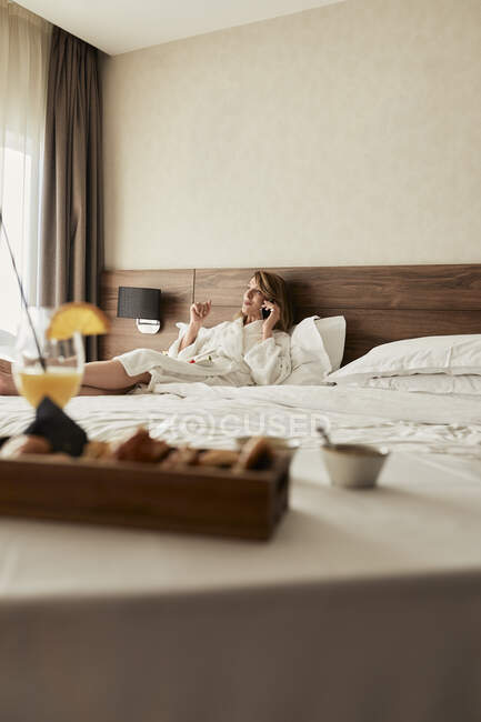Café da manhã contra a mulher falando enquanto reclinado no sofá no quarto do hotel — Fotografia de Stock