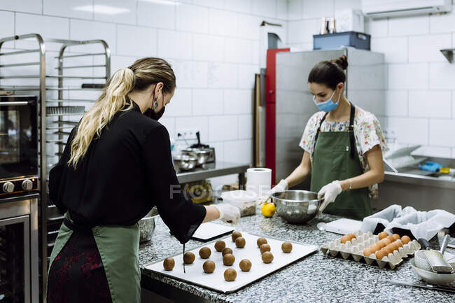 Panaderos femeninos haciendo galletas en la cocina en la panadería durante COVID-19 - foto de stock