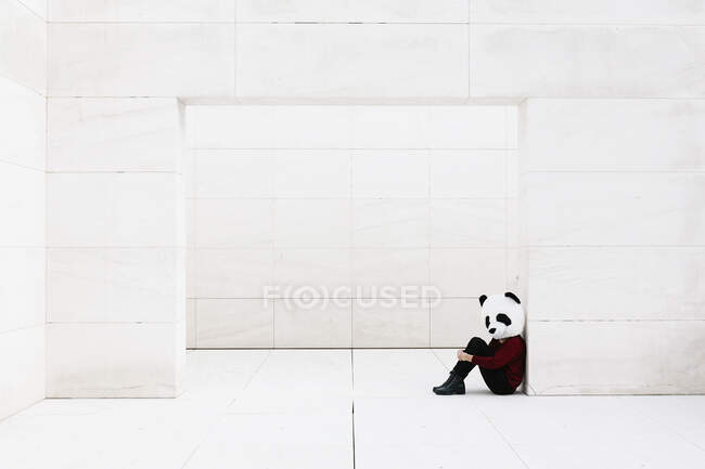 Mujer con máscara de panda sentada en la puerta contra la pared blanca - foto de stock
