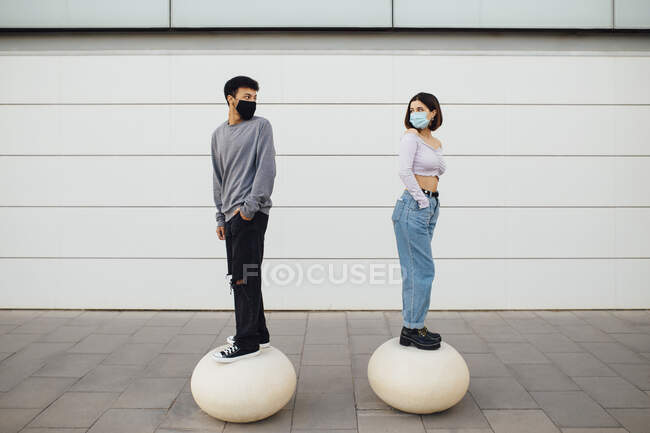 Coppia con maschera viso guardando sopra la spalla mentre in piedi su palla di cemento bianco — Foto stock