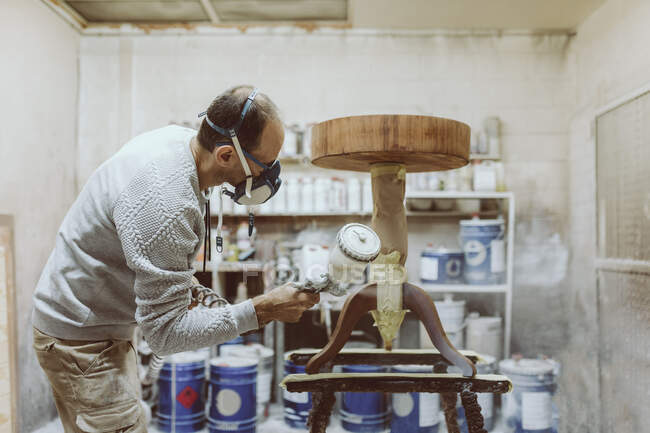 Мужчина плотник, работающий в мастерской с помощью краскового пистолета на столе — стоковое фото