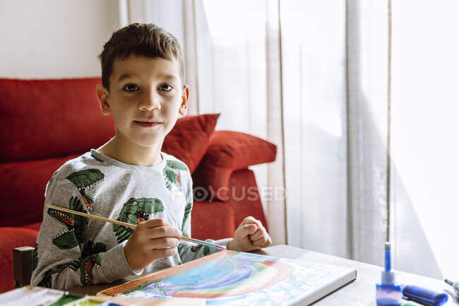 Niño con pincel por mesa en casa durante las vacaciones de verano - foto de stock